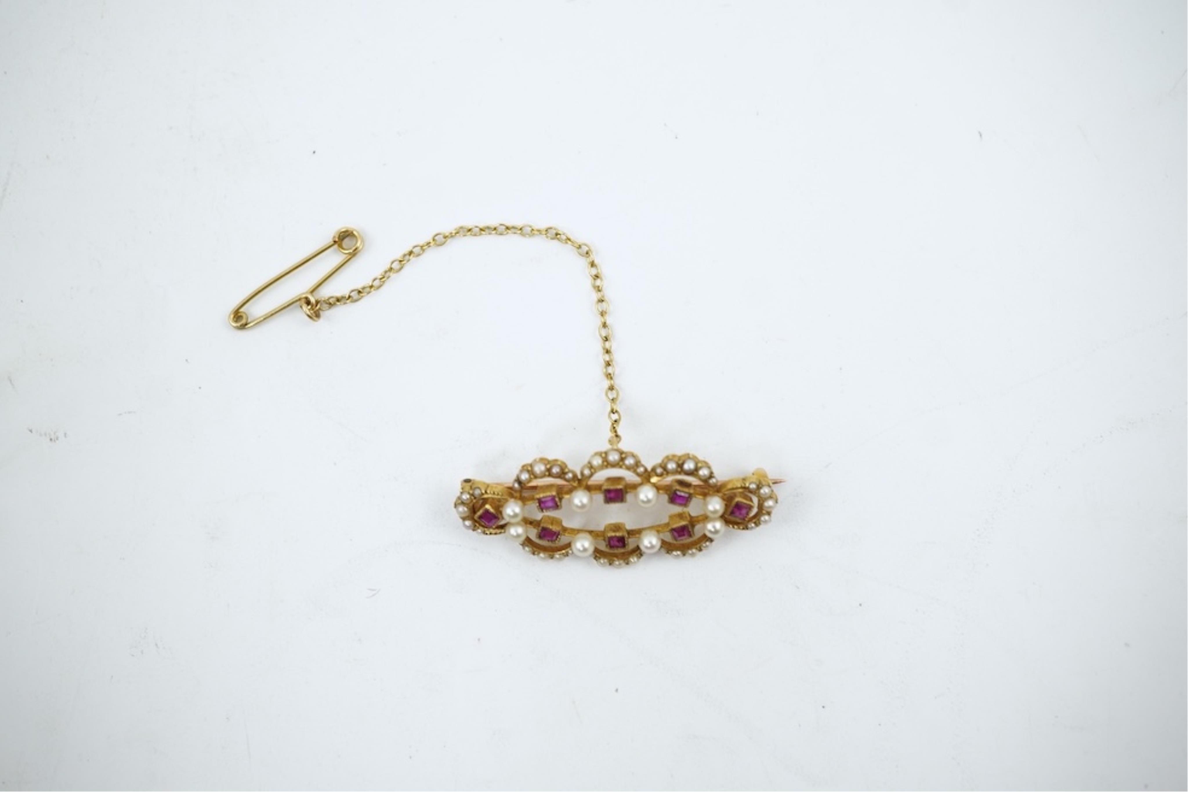 An Edwardian 15ct, ruby and seed pearl cluster set brooch, 33mm, with safety chain, gross weight 4.1 grams.